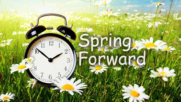 Spring Forward. An alarm clock sitting in grass with flowers.