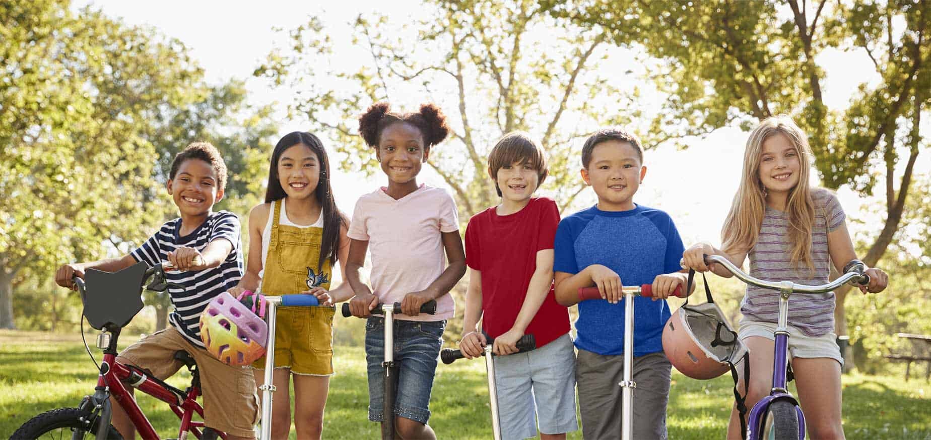 Six kids riding bicycles and scooters outside.